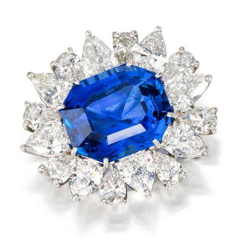 A sapphire and diamond brooch centering an octagonal-shaped step-cut sapphire, weighing 23.86 carats, within a framed surround of pear-shaped diamonds; estimated total diamond weight: 9.75 carats; mounted in platinum; length: 1 1/4in.