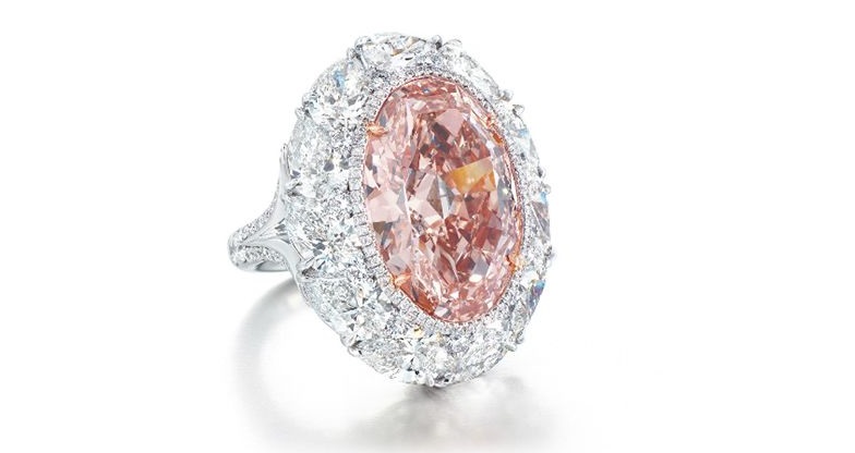 A RARE COLOURED DIAMOND AND DIAMOND RING Centering upon an oval-shaped fancy intense orangy pink diamond weighing approximately 12.85 carats, within a brilliant-cut diamond border and pear-shaped diamond surround, joined to the brilliant-cut diamond bifurcated half-hoop, mounted in platinum and 18k rose gold